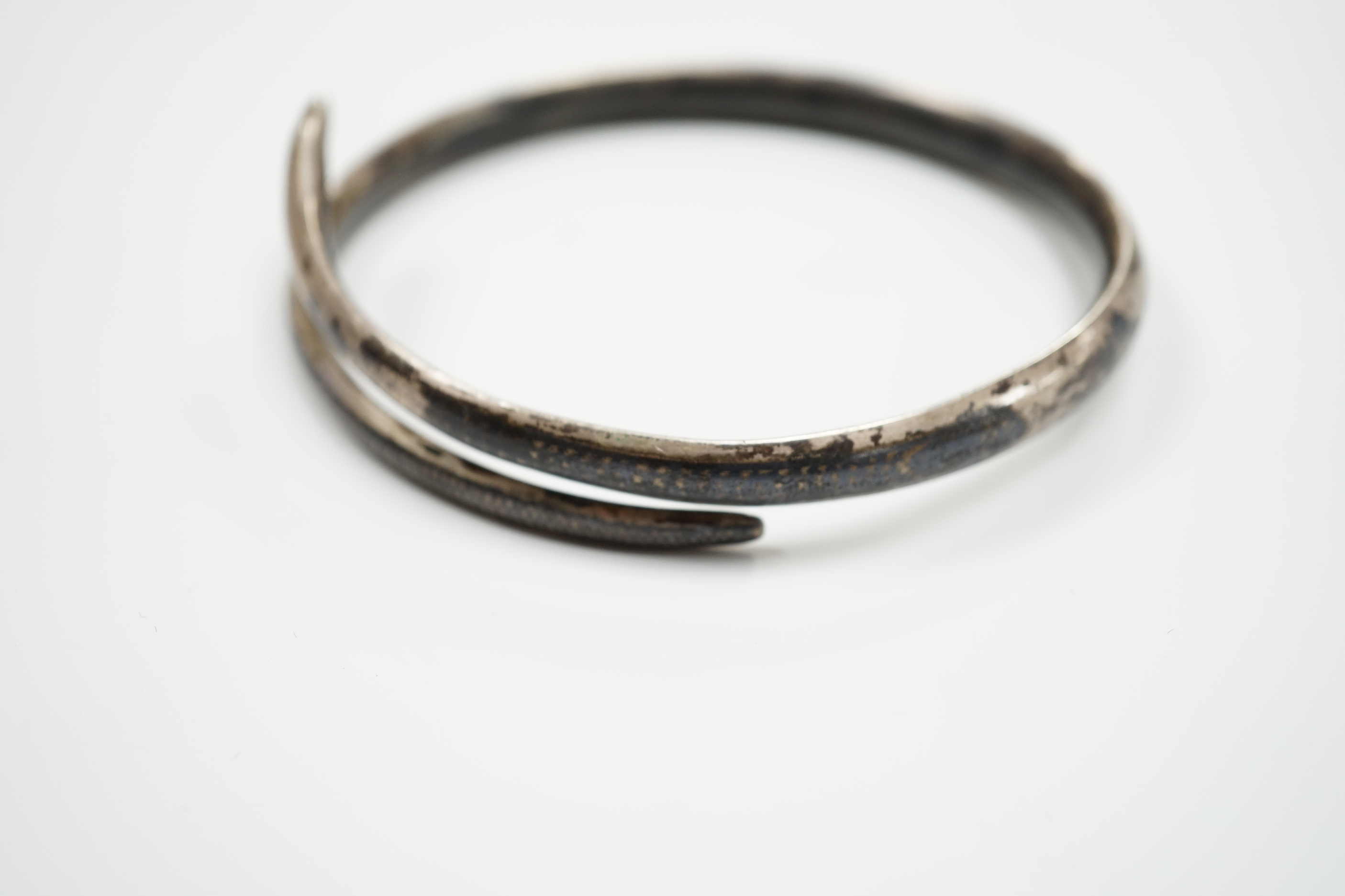 A white metal and niello serpent bangle, decorated with scene of a camel train.